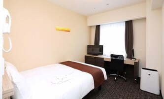 A hotel room with a bed, a desk with a computer, a TV, and a telephone.