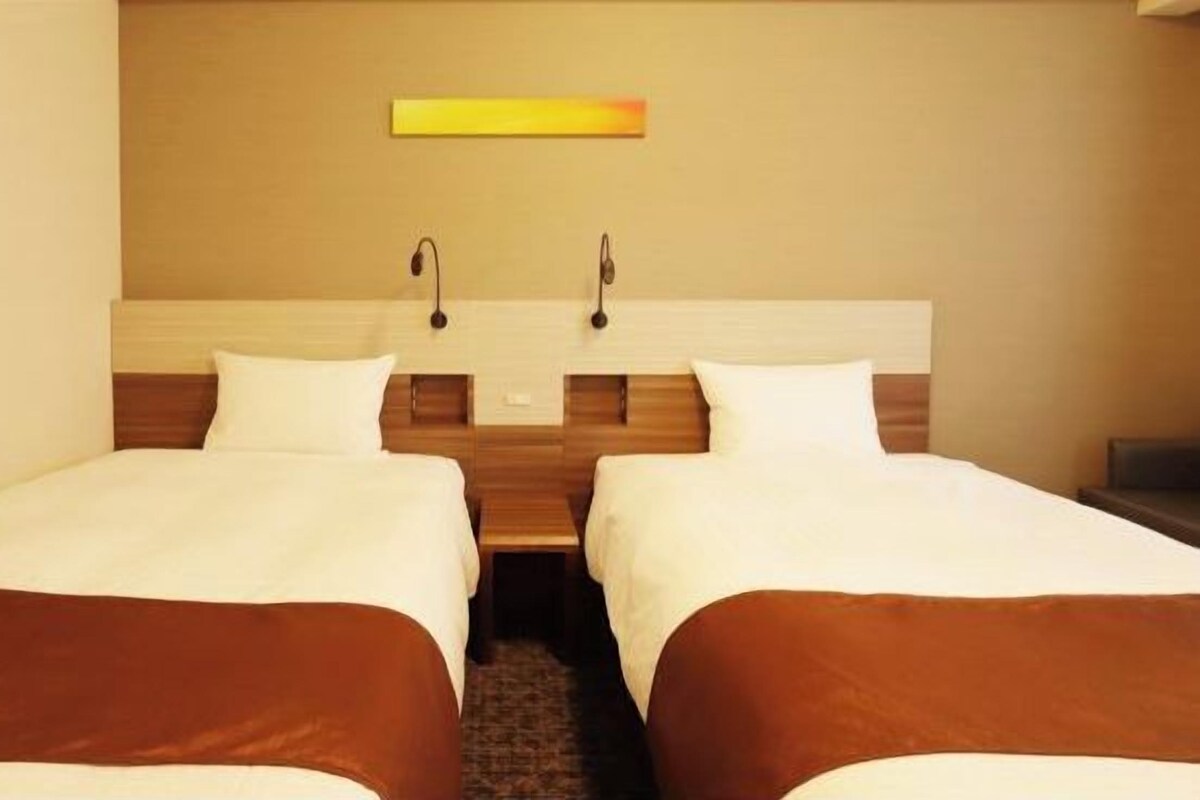 Een hotelkamer met twee enkele bedden, een houten hoofdbord en een klein nachtkastje.