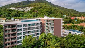 A multi-story hotel with a modern design, surrounded by lush greenery and a mountain in the background.