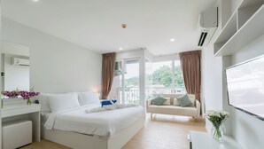 A modern hotel room with a bed, a sofa, a TV, and a balcony with curtains.