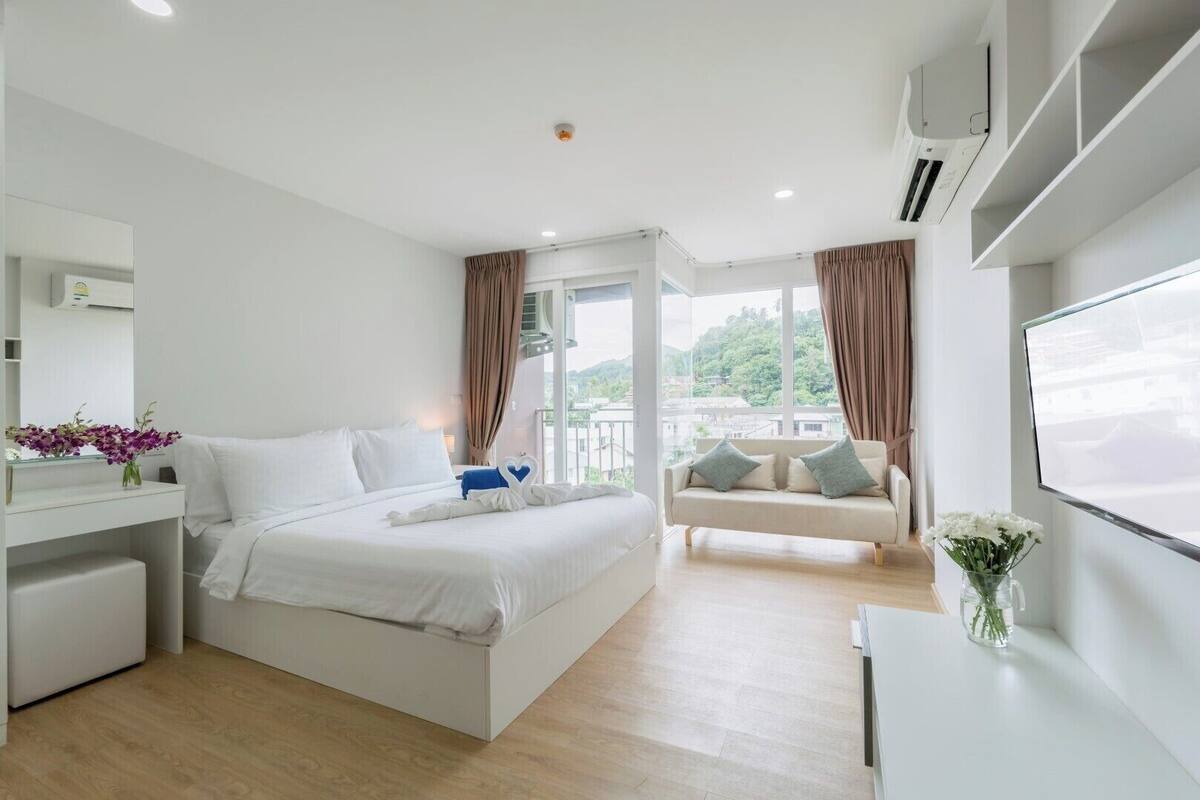 A modern hotel room with a bed, a sofa, a TV, and a balcony with curtains.