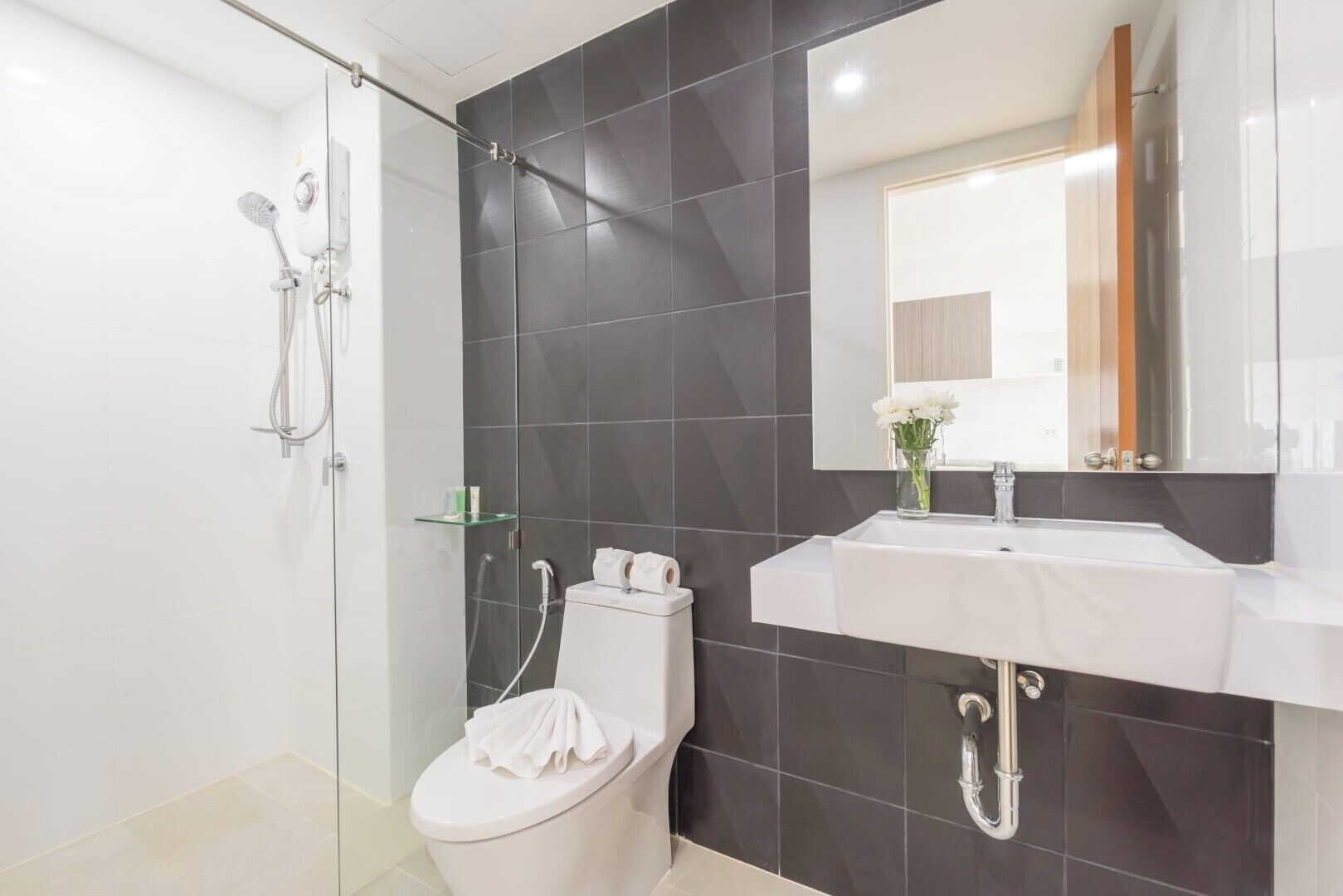 Un baño moderno con cabina de ducha de vidrio, inodoro blanco, tocador con espejo y lavabo.