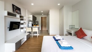 A modern hotel room with a bed, a desk, a TV, and a kitchenette.