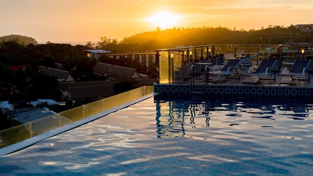 A swimming pool with lounge chairs and a glass balustrade, set against a sunset backdrop.