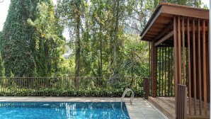 A swimming pool with a wooden deck and a covered area, surrounded by dense greenery. - Mentari Hill View 8 BR heated pool and movie room (Bandung)