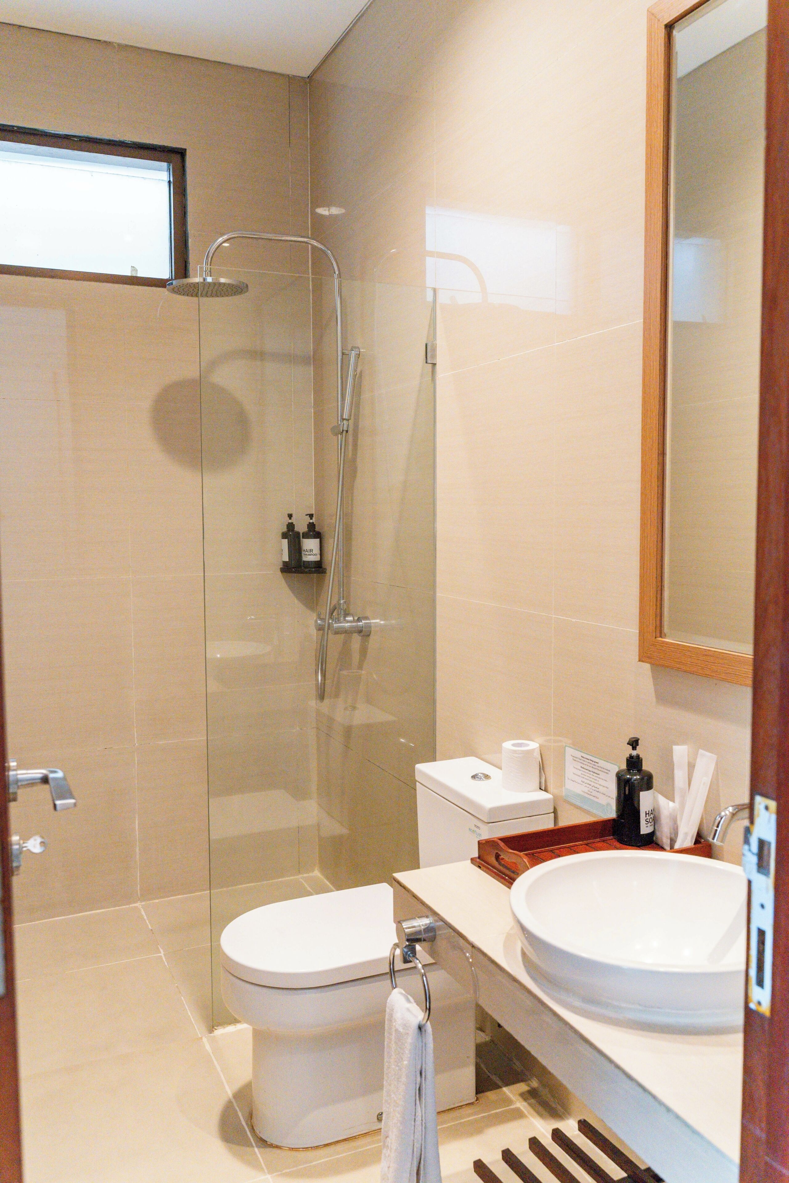 Ein modernes Badezimmer mit einer Glaskabine zur Dusche, einer weißen Toilette, einem Waschbecken mit Spiegel und Pflegeprodukten auf der Ablagefläche.