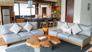 A modern living room with a grey sectional sofa, a wooden coffee table, and a kitchen in the background. - Mentari Hill View 8 BR heated pool and movie room (Bandung)