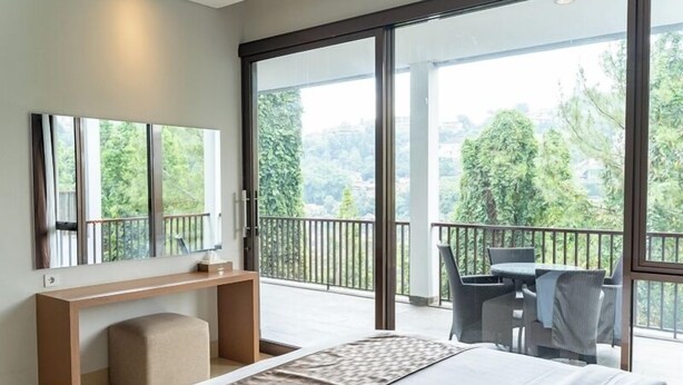 A modern hotel room with a large bed, a desk, a chair, and a balcony with a view of trees. - Mentari Hill View 8 BR heated pool and movie room (Bandung)