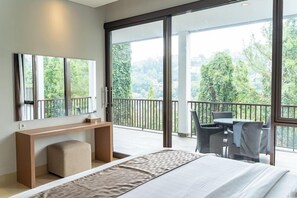 Ein modernes Hotelzimmer mit einem großen Bett, einem Schreibtisch, einem Sessel und einem Balkon mit Blick auf Bäume.