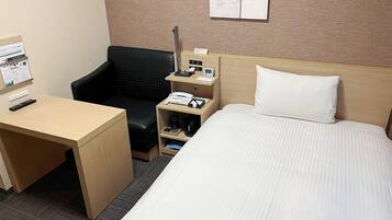 A hotel room with a bed, a desk, a chair, a nightstand with a phone and a clock, and a bulletin board with a notice.