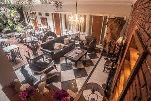 Un vestíbulo de hotel con suelo a cuadros, sofás de cuero, una araña y una zona de comedor con mesas y sillas.
