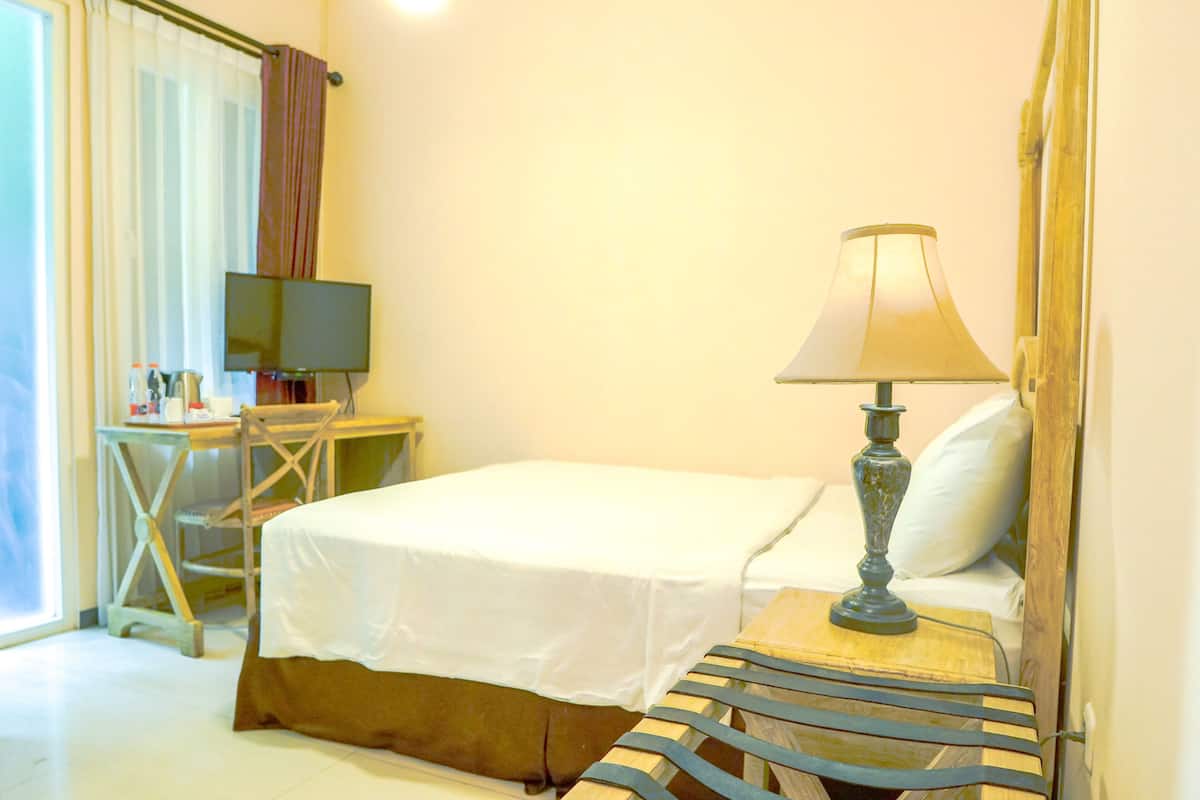 Una habitación de hotel con una cama, un escritorio con televisor y una lámpara.