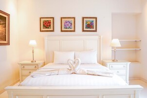 Una cama bien tendida con un arreglo de toallas con forma de corazón, ropa de cama blanca y tres cuadros florales en la pared.