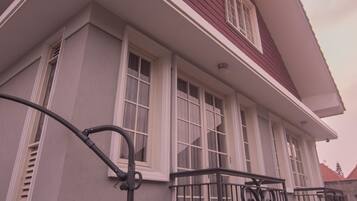 Una casa de dos pisos con balcón, detalles blancos y techo rojo.