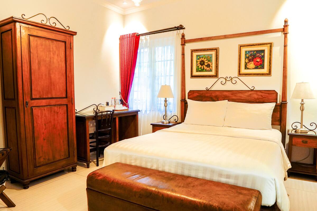 Un dormitorio con un amplio armario de madera, un escritorio con silla, una cama con ropa de cama blanca y dos lámparas fijadas a la pared.