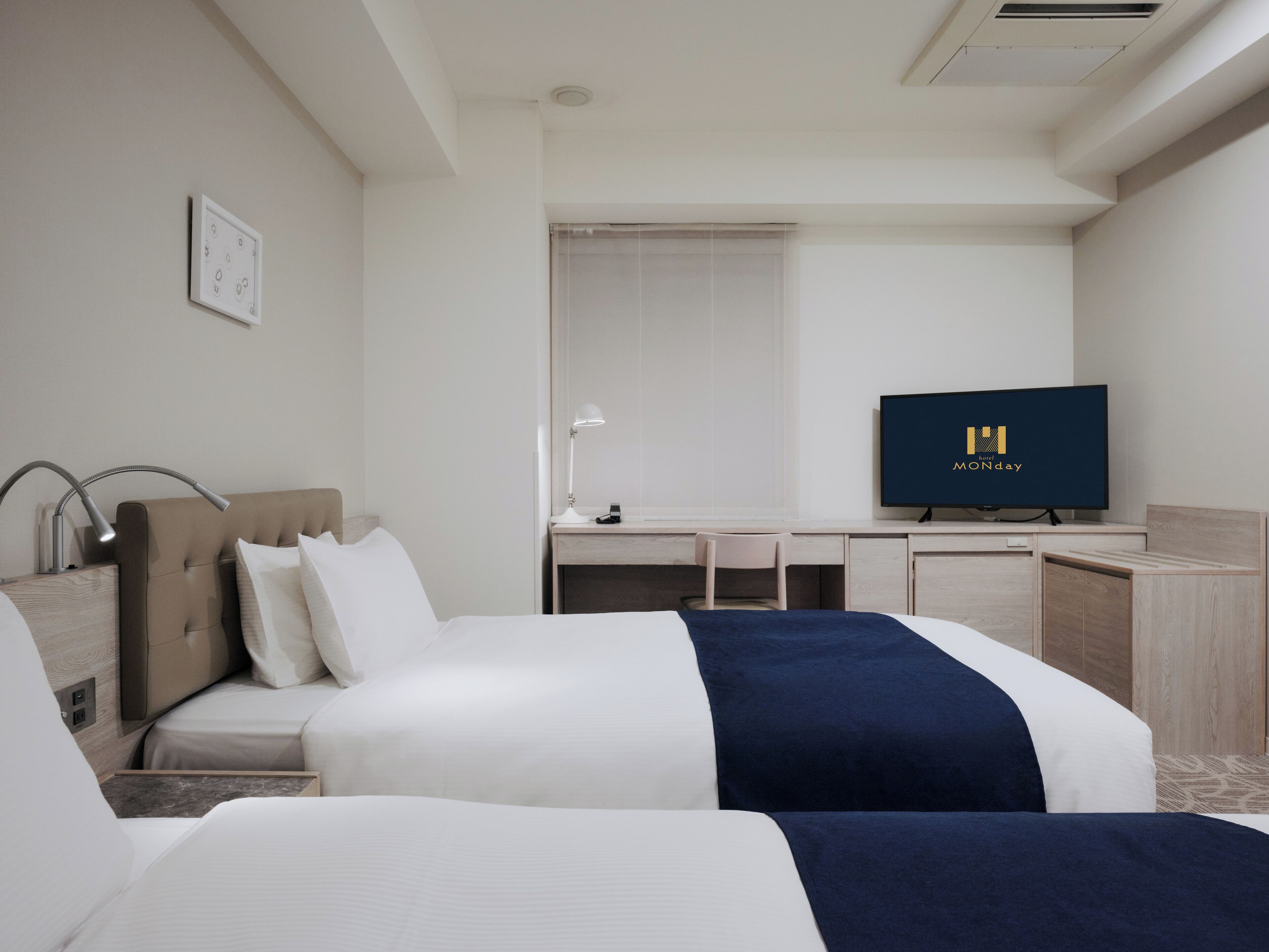 A hotel room with two beds, a desk, a chair, a TV, and a window.