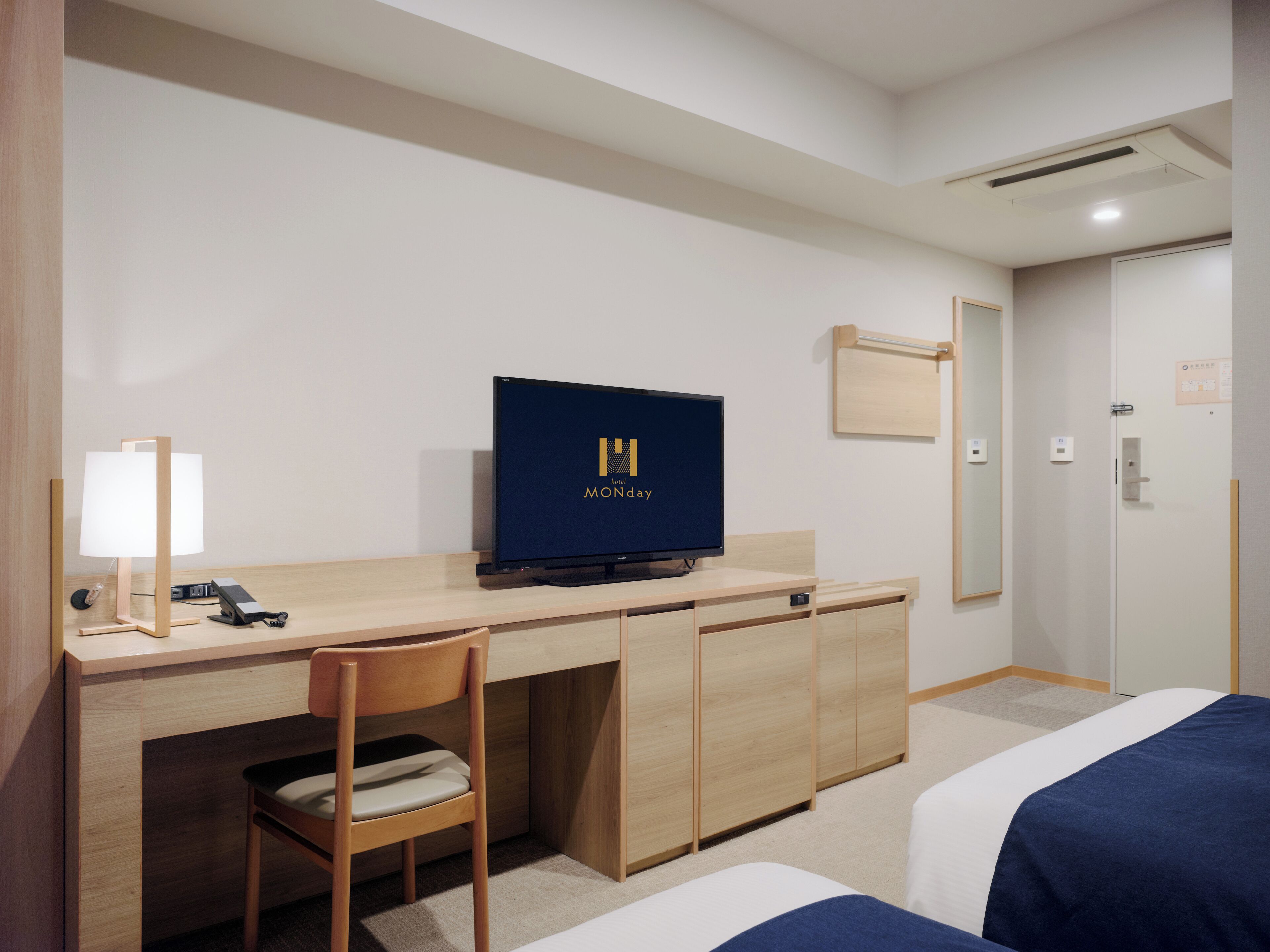 A hotel room with a wooden desk, a television, a chair, and a bed with blue bedding.
