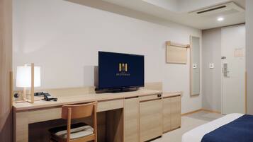 A hotel room with a wooden desk, a television, a chair, and a bed with blue bedding.
