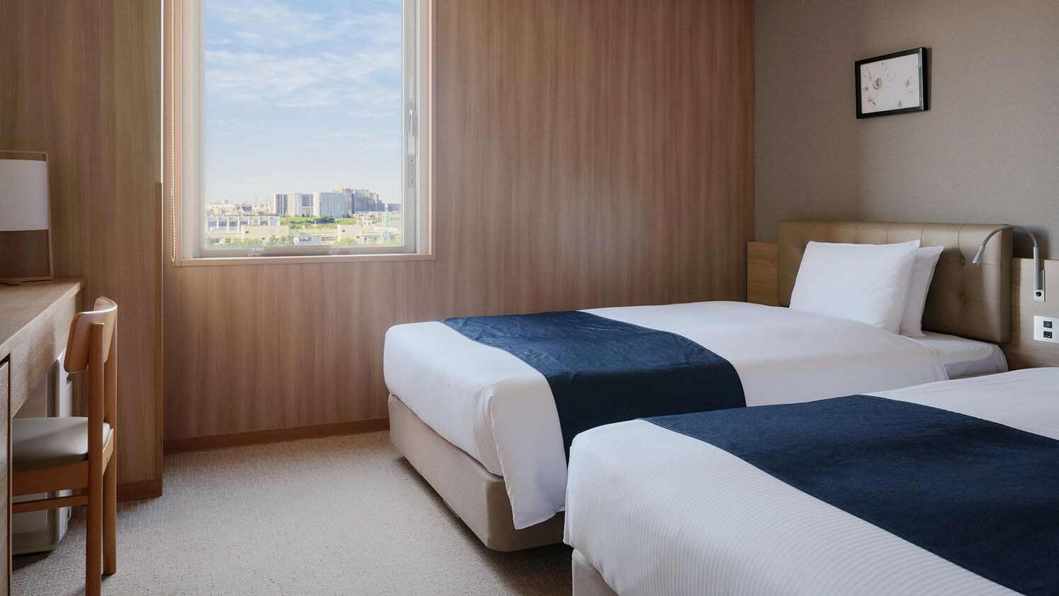 A hotel room with two beds, a desk, a chair, and a large window with a city view.