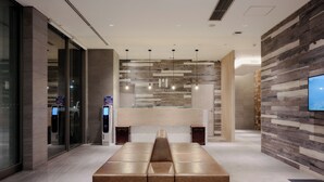 A modern lobby with a central seating area, a reception desk, and a mounted television. - Hotel MONday Haneda Airport (Tokyo)