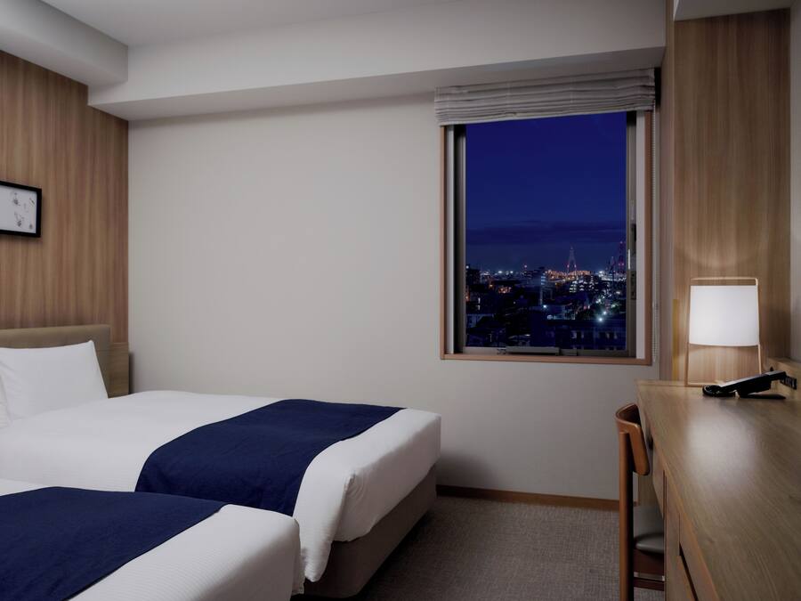 Een hotelkamer met twee bedden, een bureau, een lamp en een raam met uitzicht op de stad.