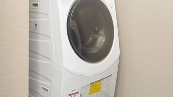 A front-loading washing machine with a control panel, a water inlet hose, and a drain hose.