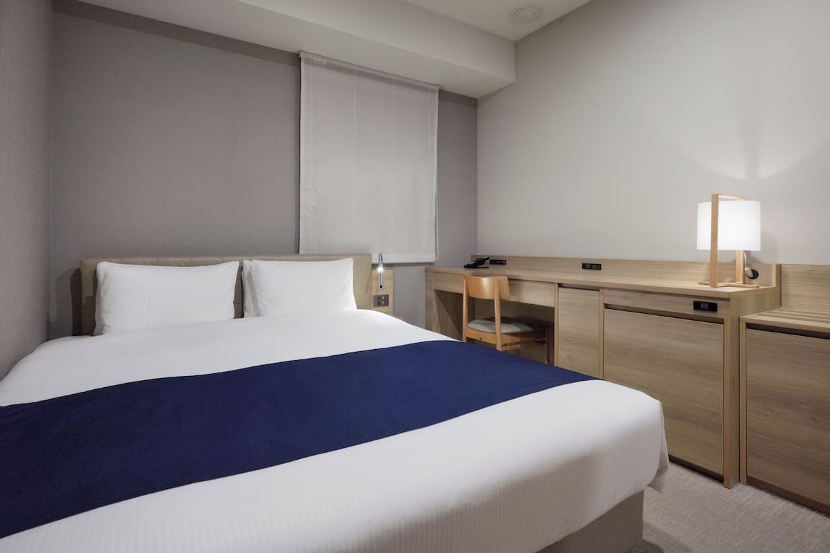 A hotel room with a large bed, a desk with a lamp, and a chair.