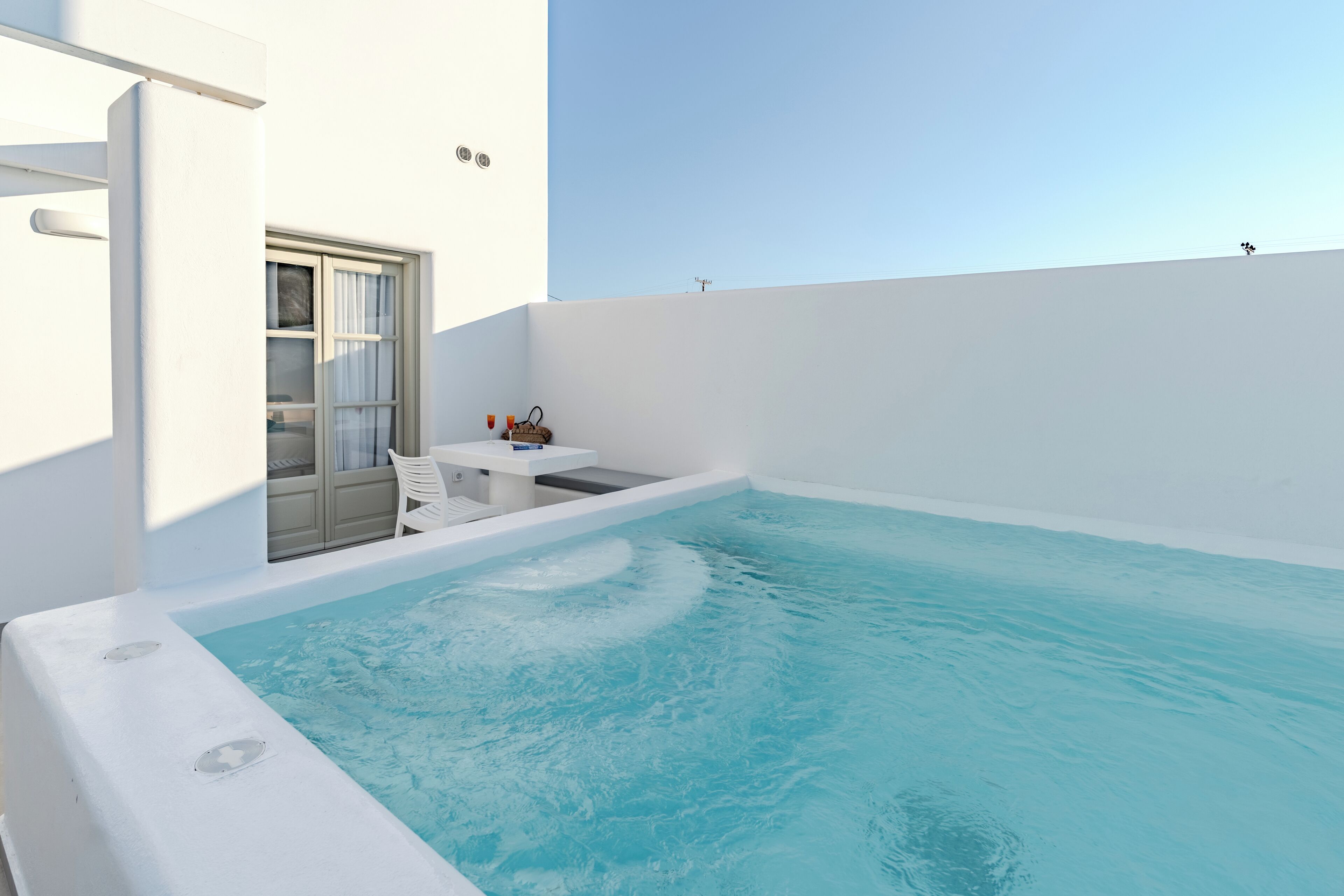 A modern outdoor swimming pool with a white interior and a clear blue sky in the background.
