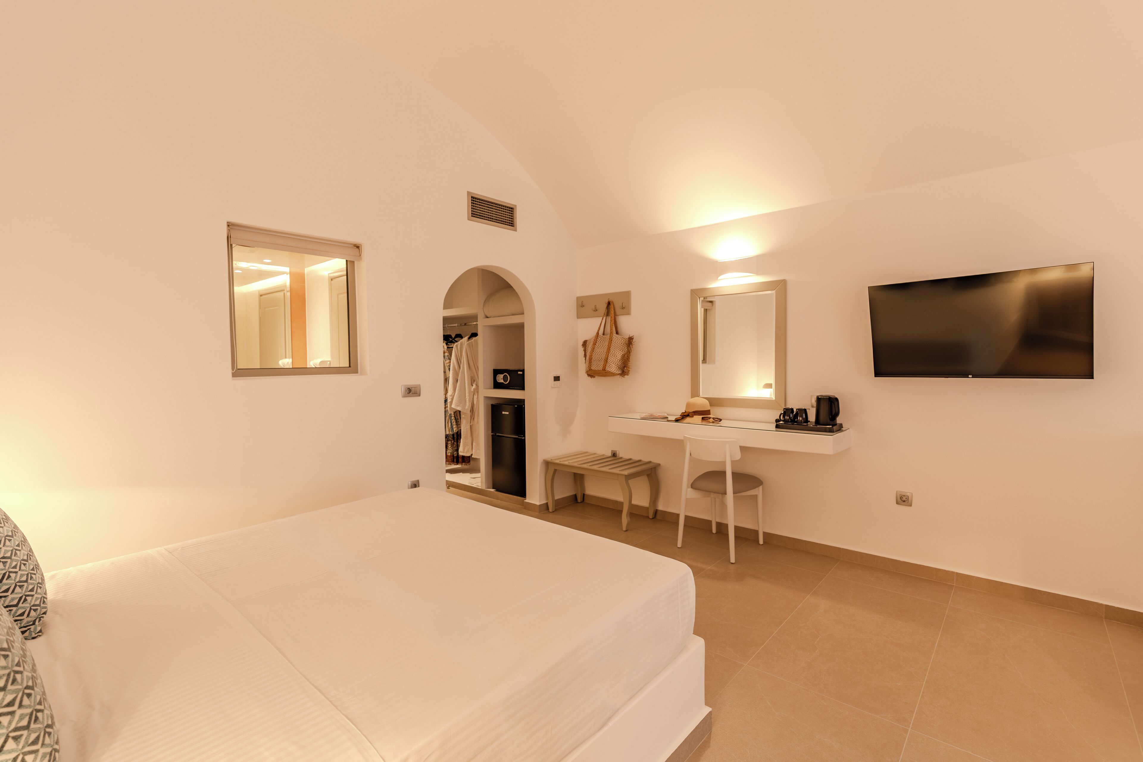 Una habitación de hotel con cama, escritorio, silla, televisor y armario.