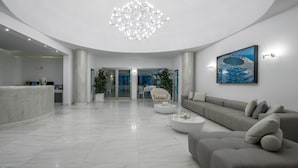 A modern lobby with a reception desk, a grey sofa, a coffee table, and a chandelier.