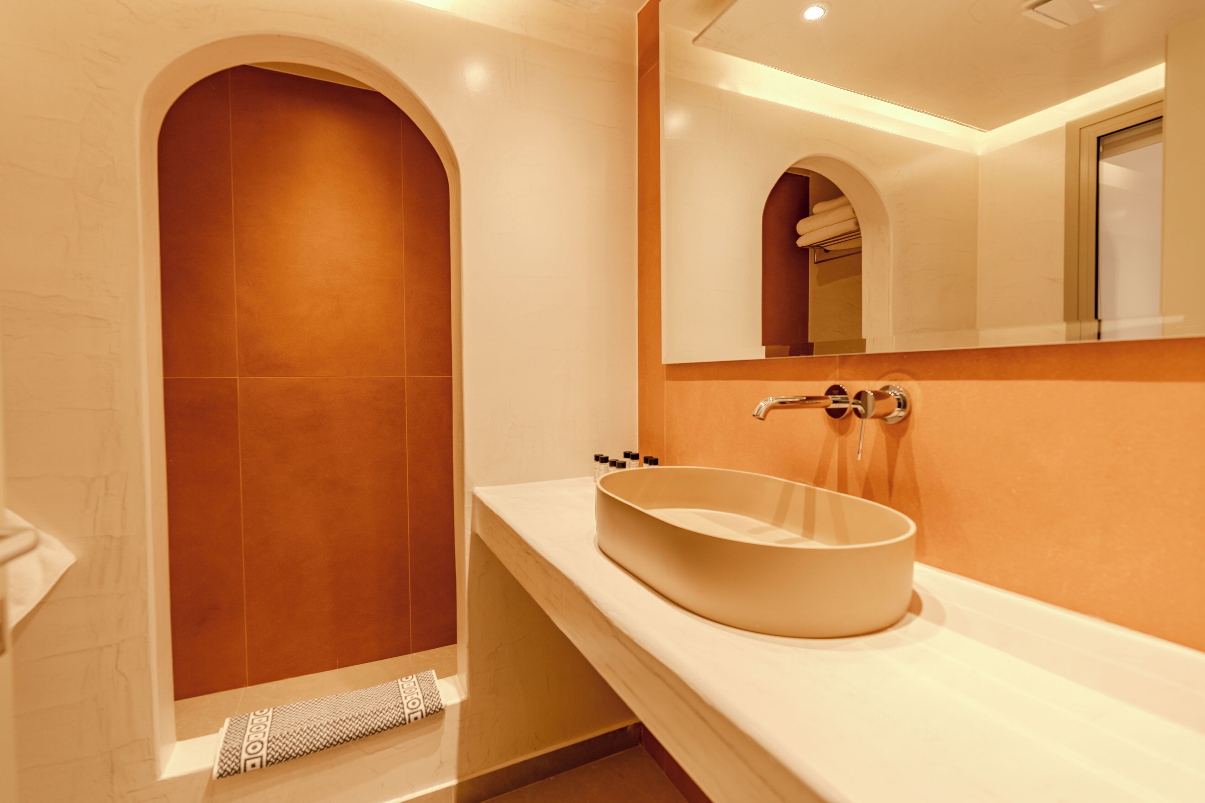 Une salle de bain moderne avec une grande porte en arc, un lavabo rond posé sur un meuble et un miroir au-dessus.