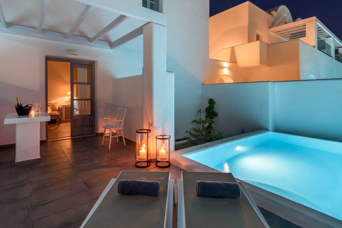 Uma área moderna com piscina ao ar livre, cadeiras de descanso e velas, espaço de estar com mesa e cadeiras, e vista para a arquitetura do edifício.