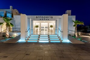 A modern hotel entrance with a staircase leading up to the doors, palm trees, and a clear sky. - Antoperla Luxury Hotel & Spa (Santorini)