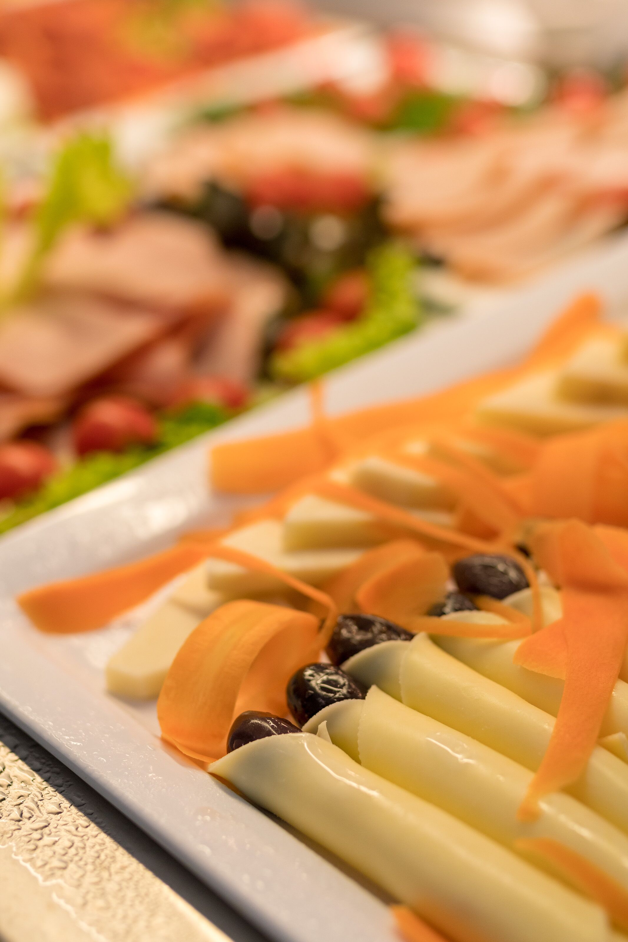 A close-up of a food platter with various items including sliced carrots, cheese, and olives.
