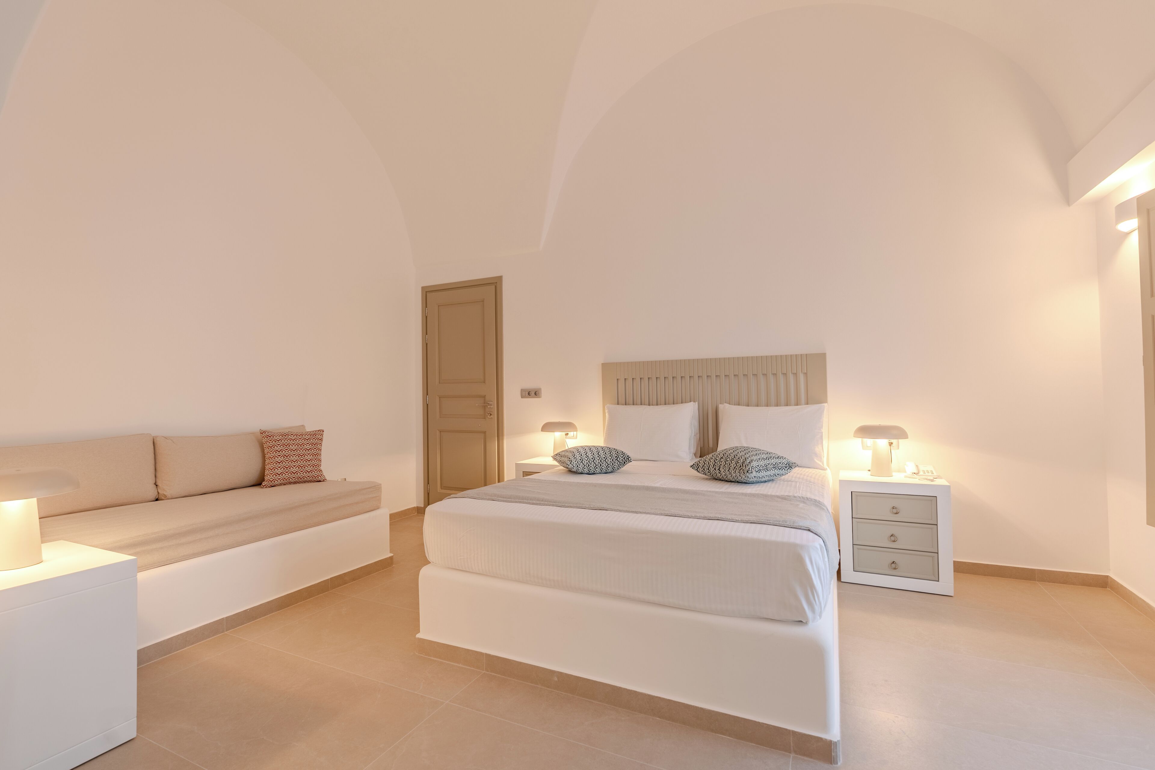A bedroom with a bed, a sofa, a nightstand, and a door.