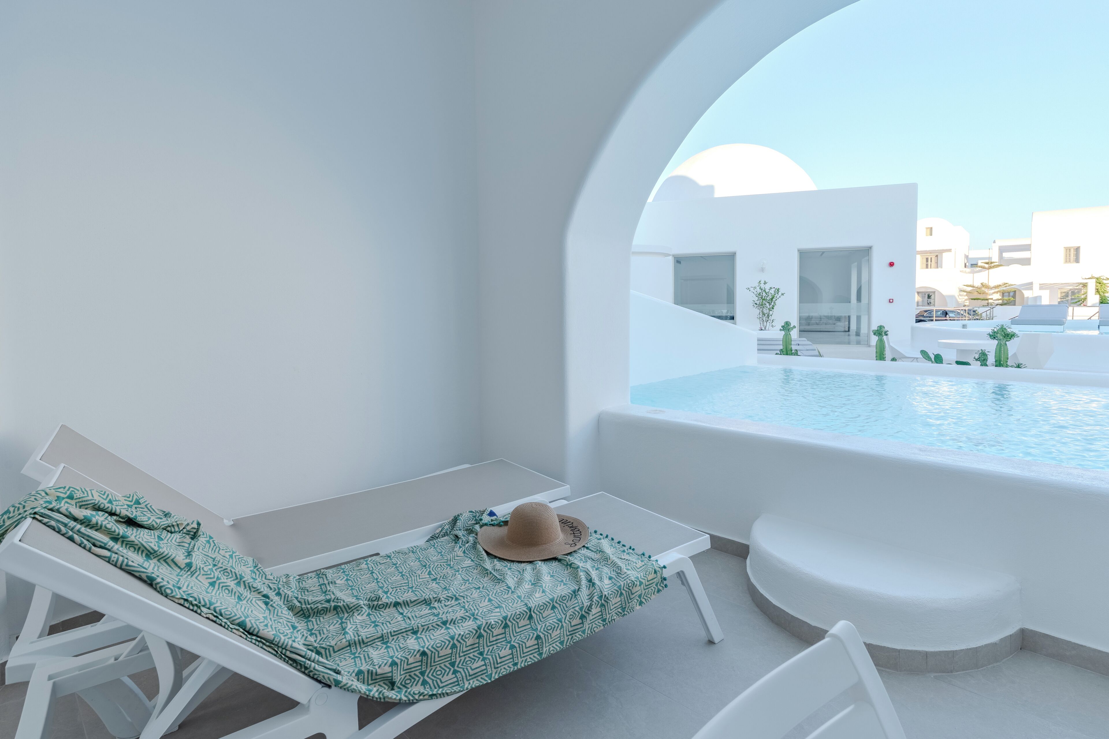 A balcony with a white pool, a lounge chair, and a table with a patterned cloth.