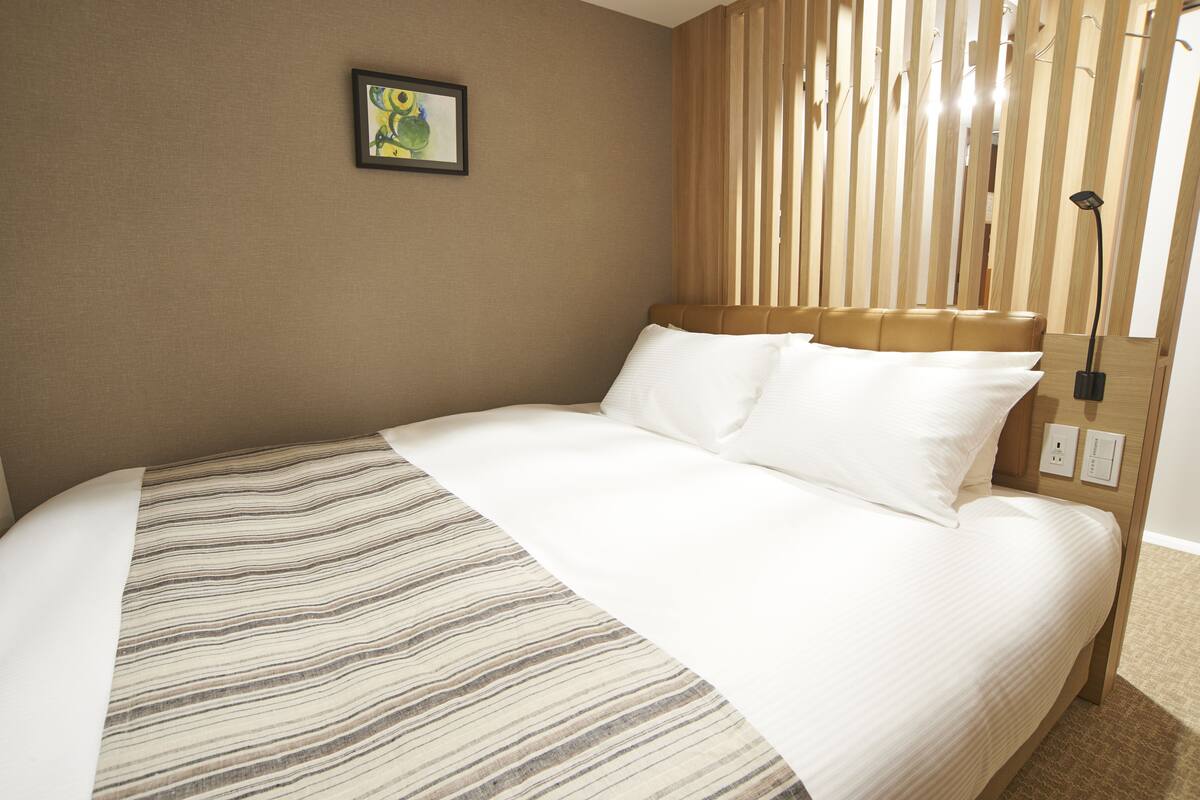 A neatly made bed with a striped bedspread, a headboard with vertical slats, and a framed picture on the wall.