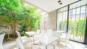 A modern outdoor dining area with white furniture and a view of greenery through large windows. - Quintessa Hotel Tokyo Haneda Comic & Books (Tokyo)
