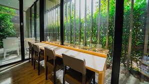 A modern dining area with a long table and chairs, large windows with a view of greenery and buildings. - Quintessa Hotel Tokyo Haneda Comic & Books (Tokyo)