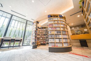 A modern library with curved bookshelves, a seating area, and large windows. - Quintessa Hotel Tokyo Haneda Comic & Books (Tokyo)