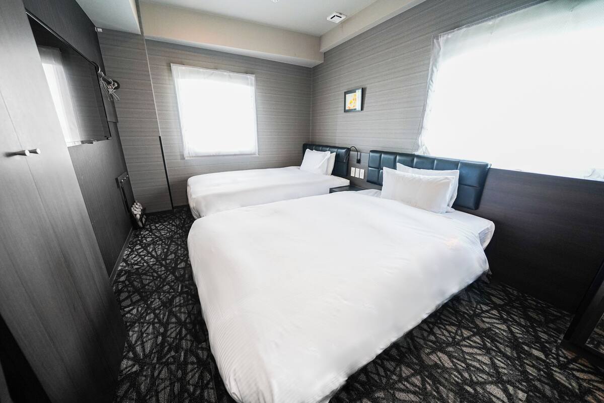 A hotel room with two beds, a large window, and a patterned carpet.