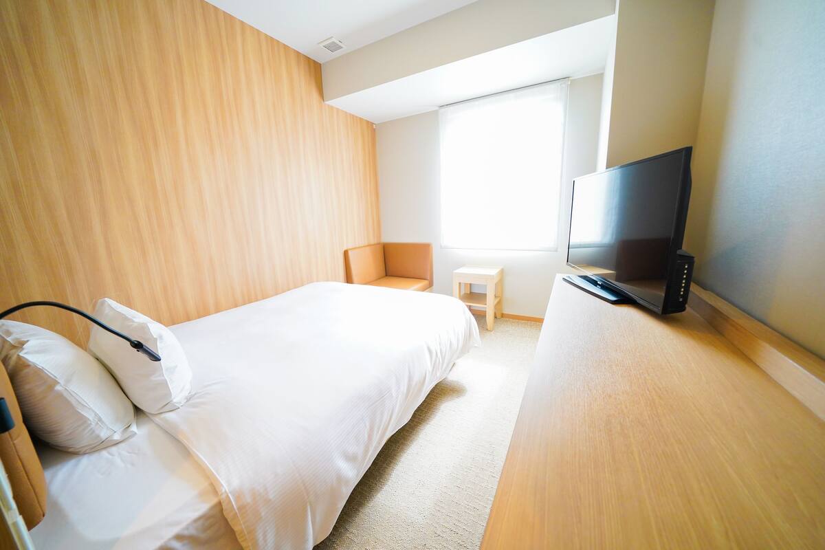 A hotel room with a bed, a television, a chair, and a small table.