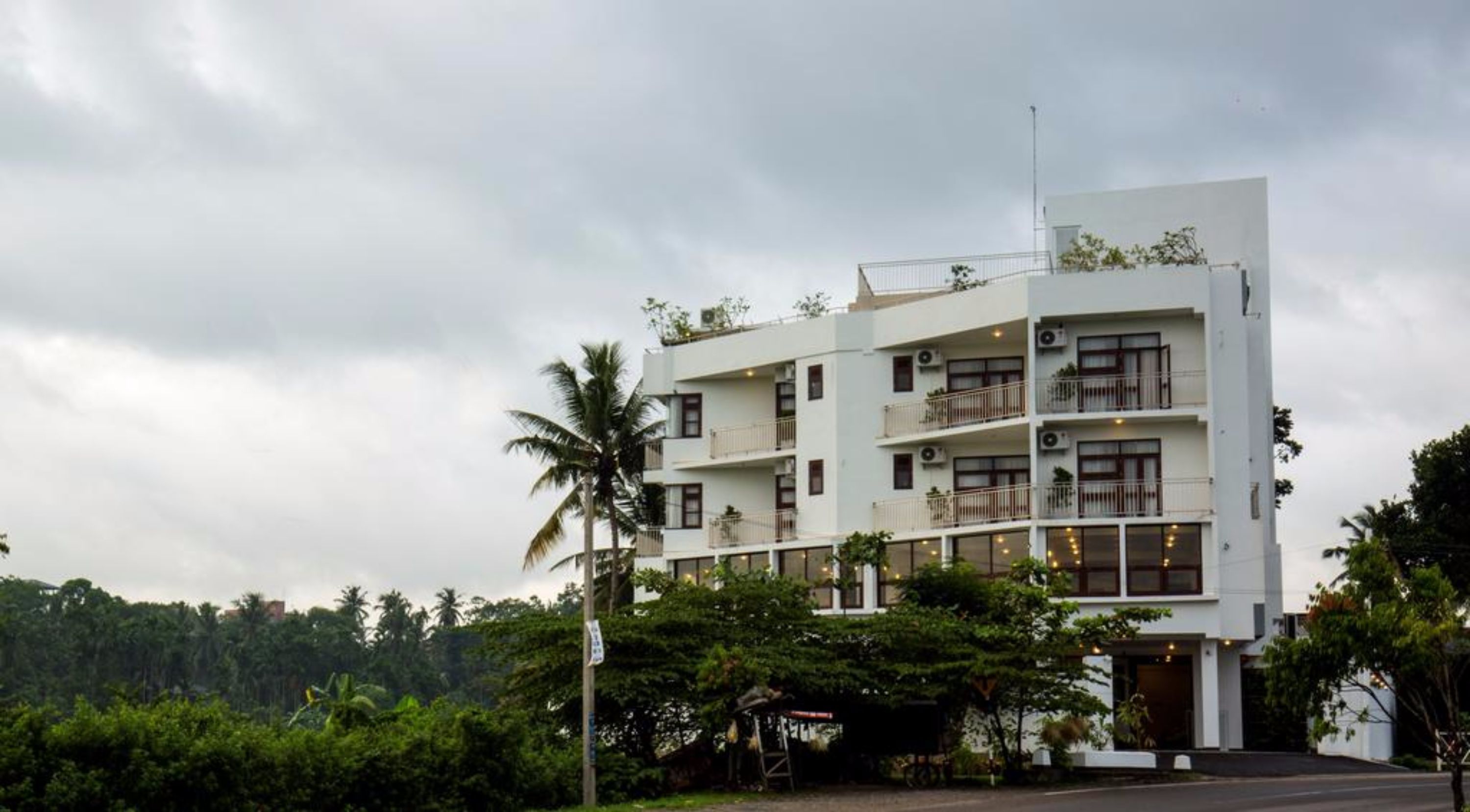 Un immeuble à plusieurs étages doté de balcons, de climatiseurs et d’un toit plat agrémenté de plantes.