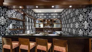 Un espace bar avec un papier peint à motifs, un comptoir en bois et trois tabourets de bar.