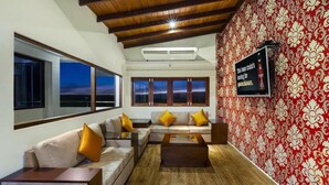 Un salon moderne avec un grand ensemble de canapés, une table basse et un téléviseur fixé au mur. De grandes fenêtres offrent une vue sur l’extérieur.