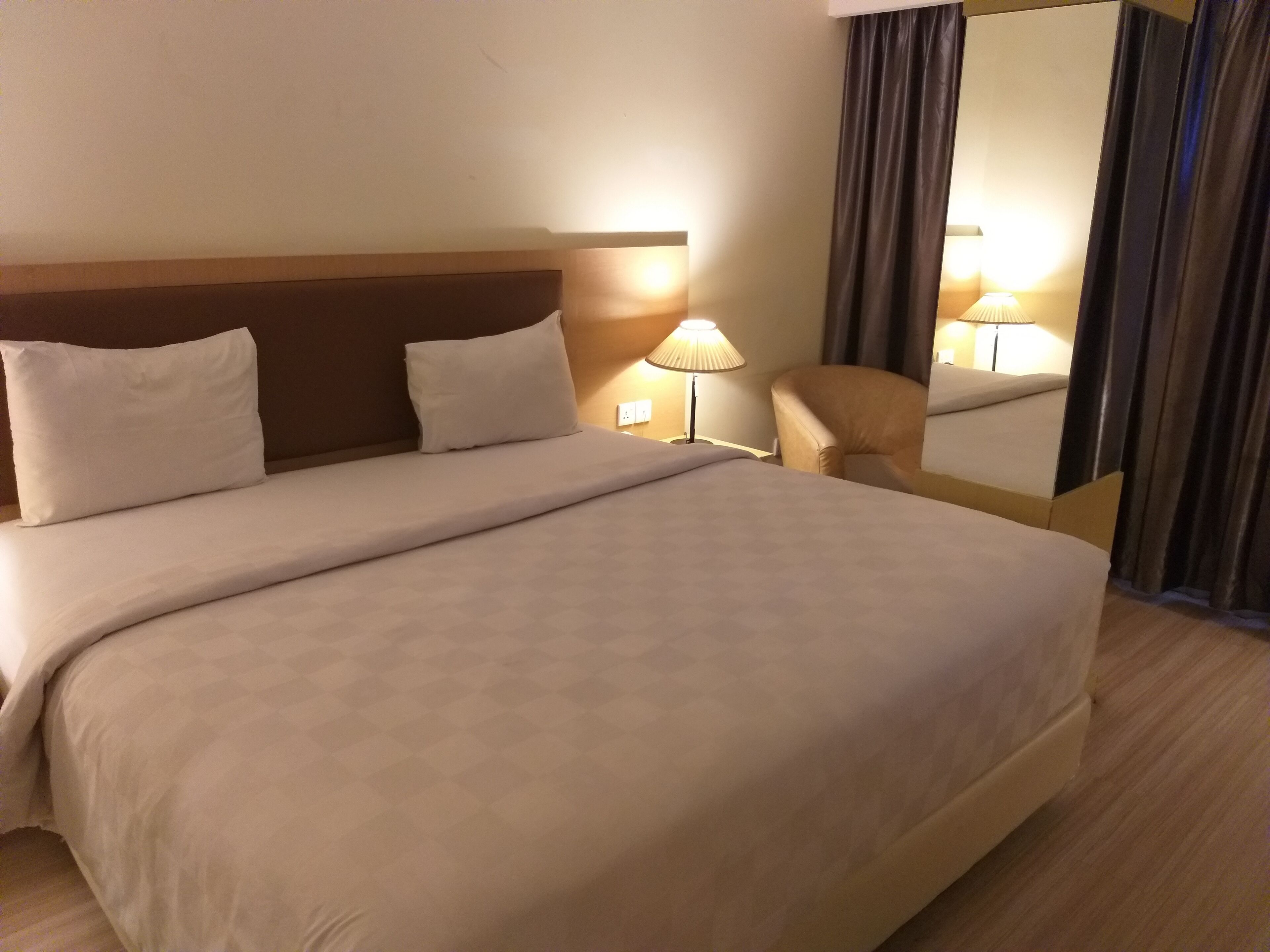 Una habitación de hotel con una cama grande, una mesita de noche con lámpara, una silla y un espejo.