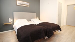 A double bed with a grey headboard and two dark-colored bedspreads, a bedside table with a lamp, and a framed picture on the wall. - Napoli resturant & Hotell (Alstahaug)