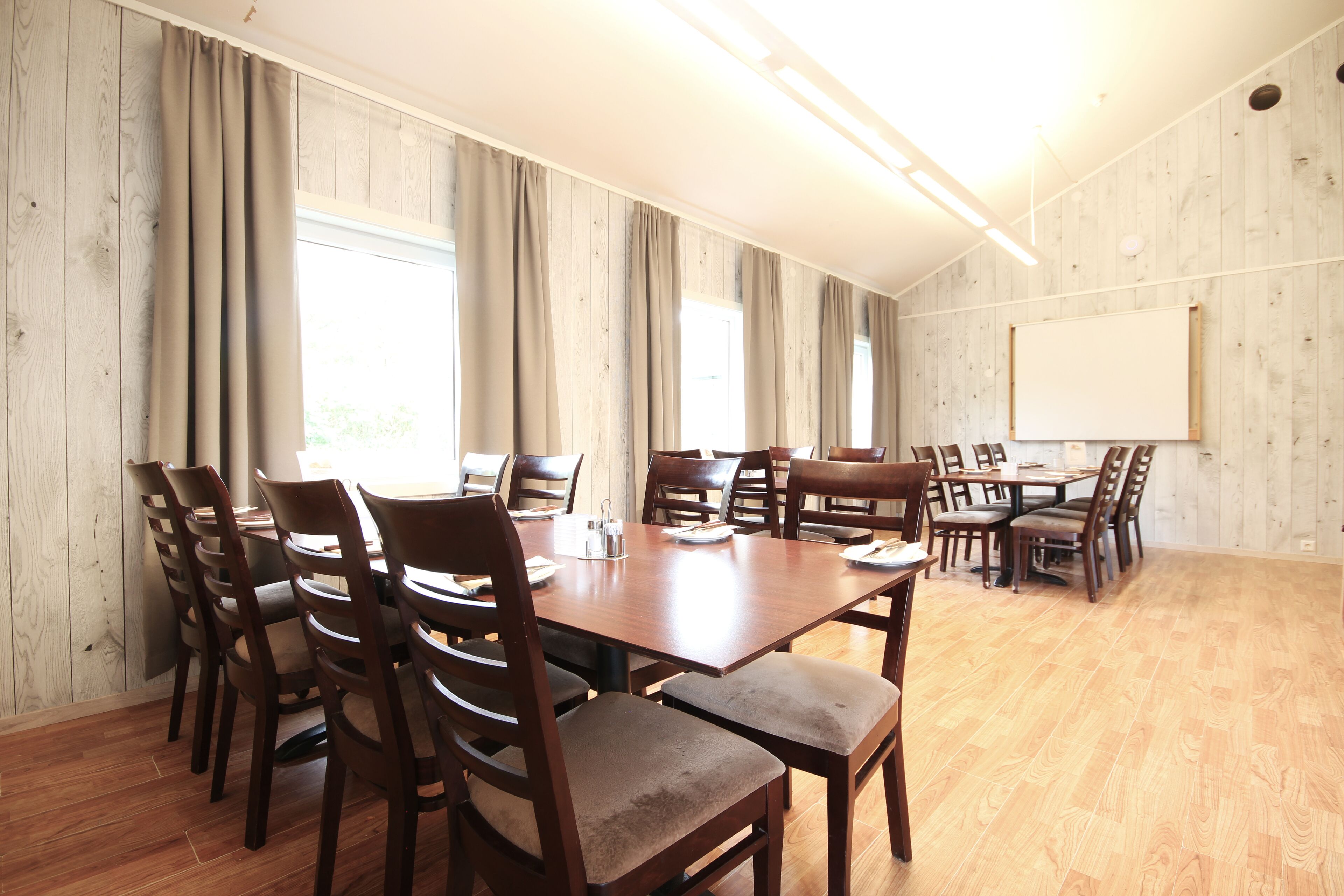 A conference room with wooden flooring, a large table surrounded by chairs, and a whiteboard on the wall.