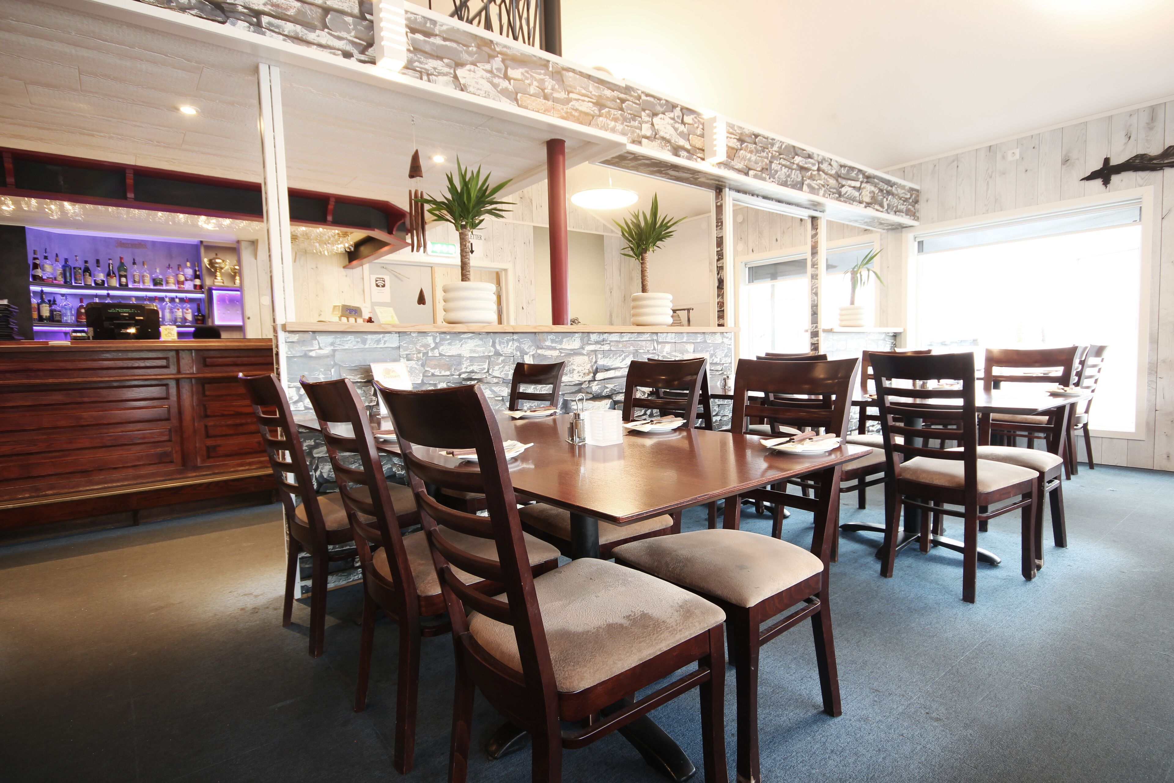 A dining area with a large wooden table and multiple chairs, a stone accent wall, and a bar area with shelves of bottles.