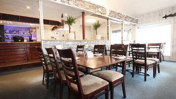 A dining area with a large wooden table and multiple chairs, a stone accent wall, and a bar area with shelves of bottles.
